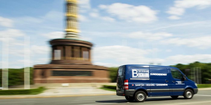 Der Lieferwagen von Bergmann Kundendienst ist in Bewegung, während die goldene Statue im Hintergrund verschwommen erscheint.