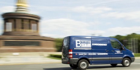 Ein blauer Lieferwagen fährt schnell vorbei, während im Hintergrund ein monumentales Gebäude mit goldenen Details sichtbar ist.